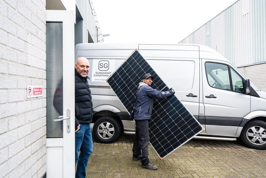 Statushouder Msgina Albraha draagt een zonnepaneel. Hij is met een collega aan het werk bij Sungarant. Via het STT is hij uitgestroomd naar deze reguliere baan. 