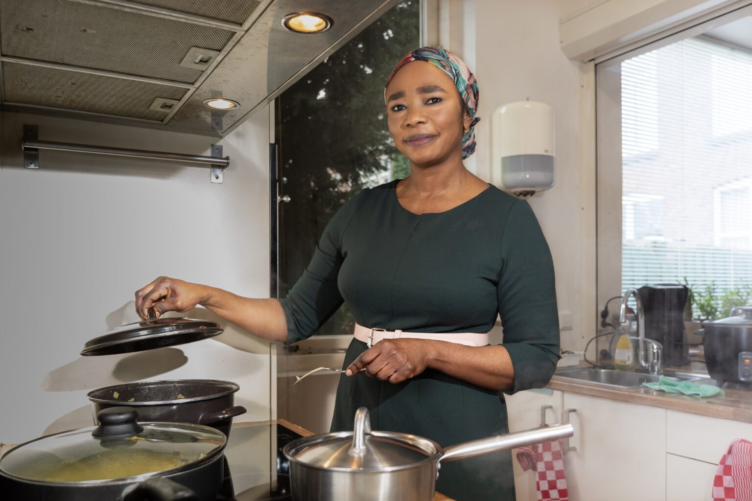 Een oud-deelneemster de Leerlijn Zorg staat achter een fornuis en tilt een deksel van een pan.