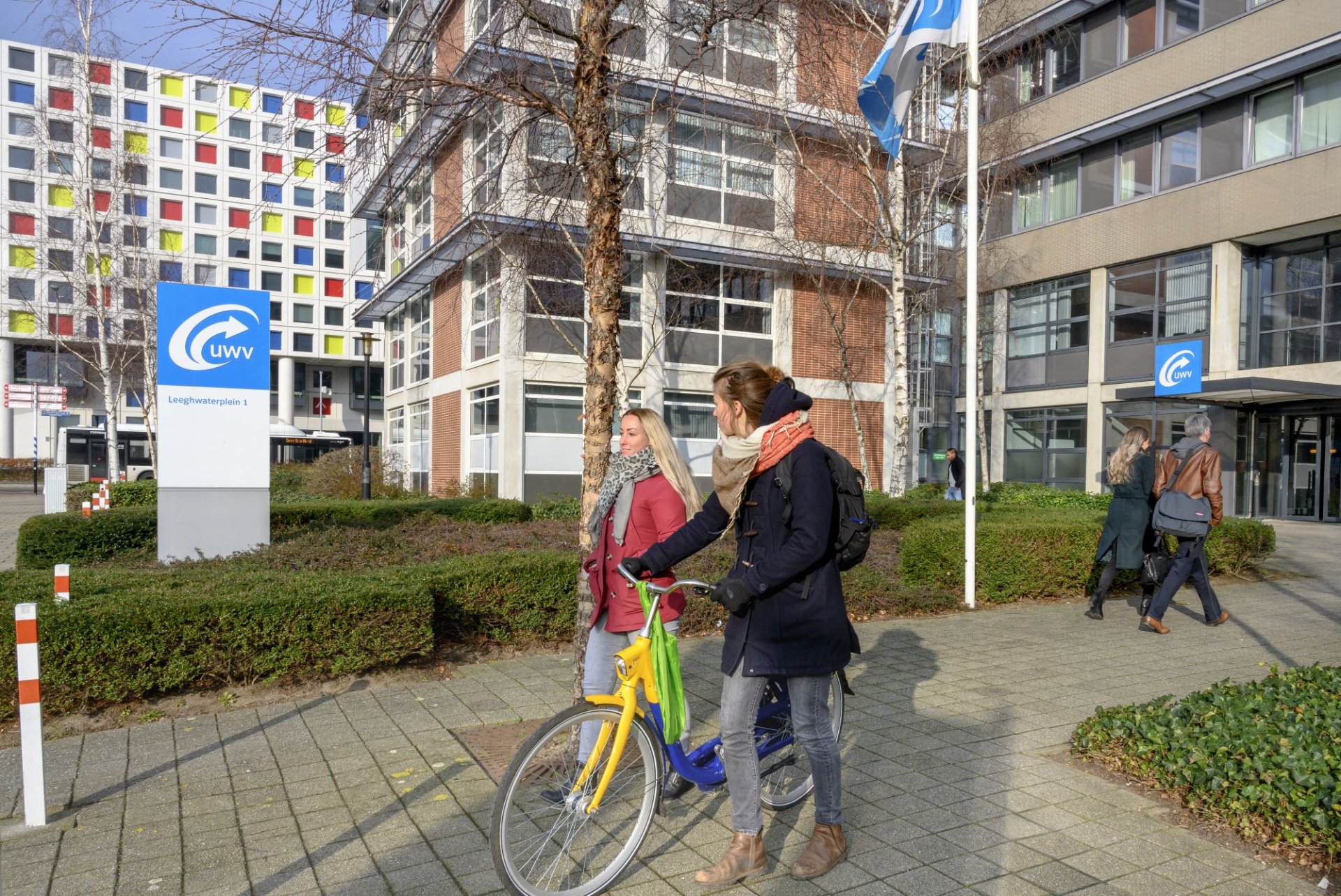 2 mensen met een fiets lopen weg van het kantoor van UWV in Den Haag, 2 anderen lopen ernaartoe