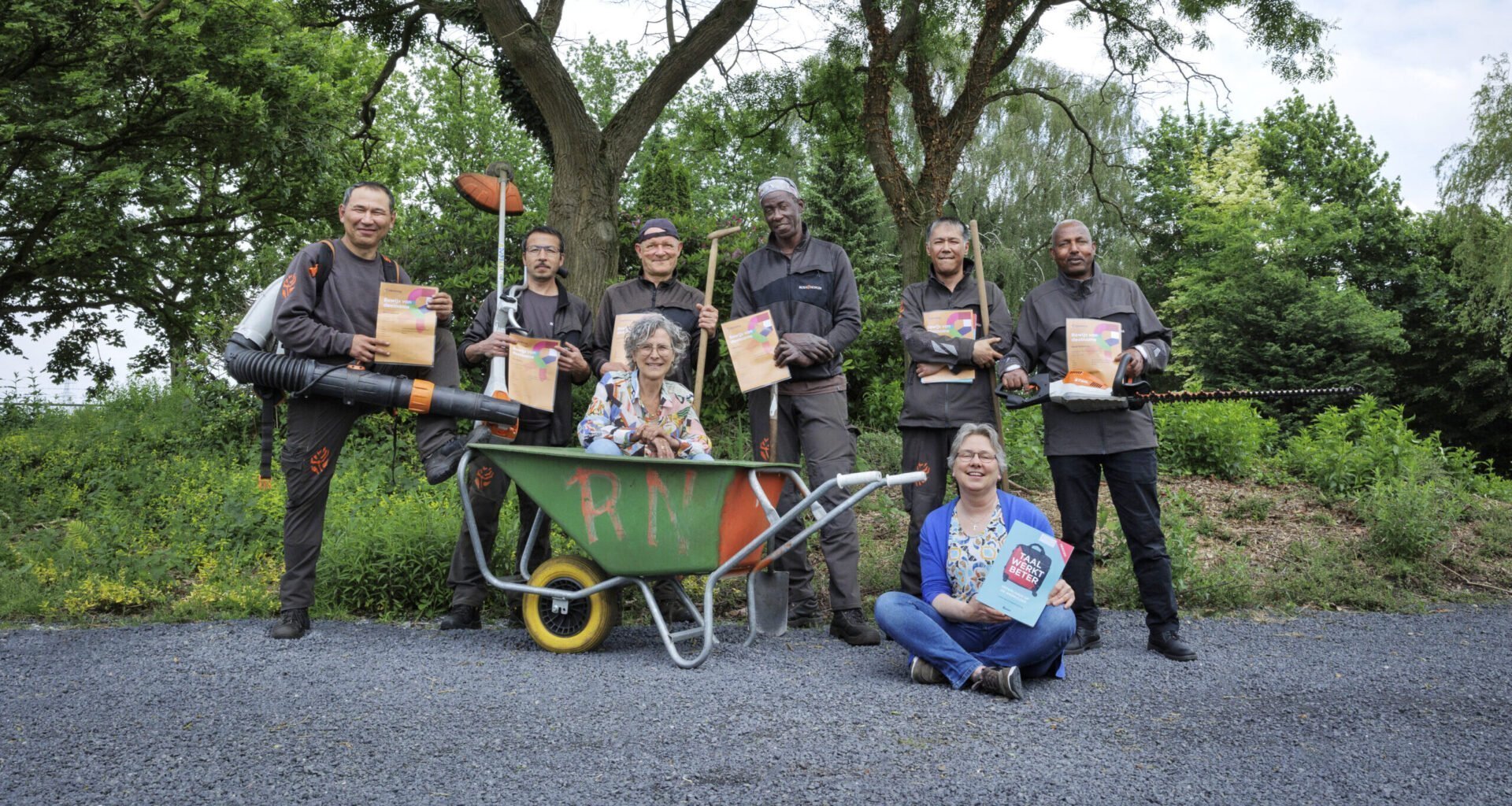 Werknemers met tuingeredschap in de hand, zitten in en staand achter een kruiwagen