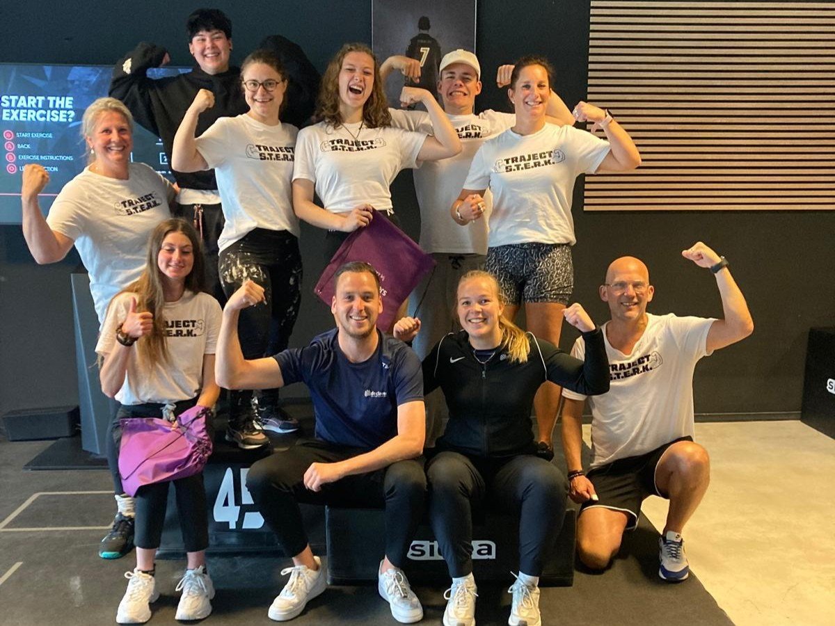 vrolijke groepsfoto van deelnemers en coaches van traject STERK laten in een gymzaal hun spierballen zien