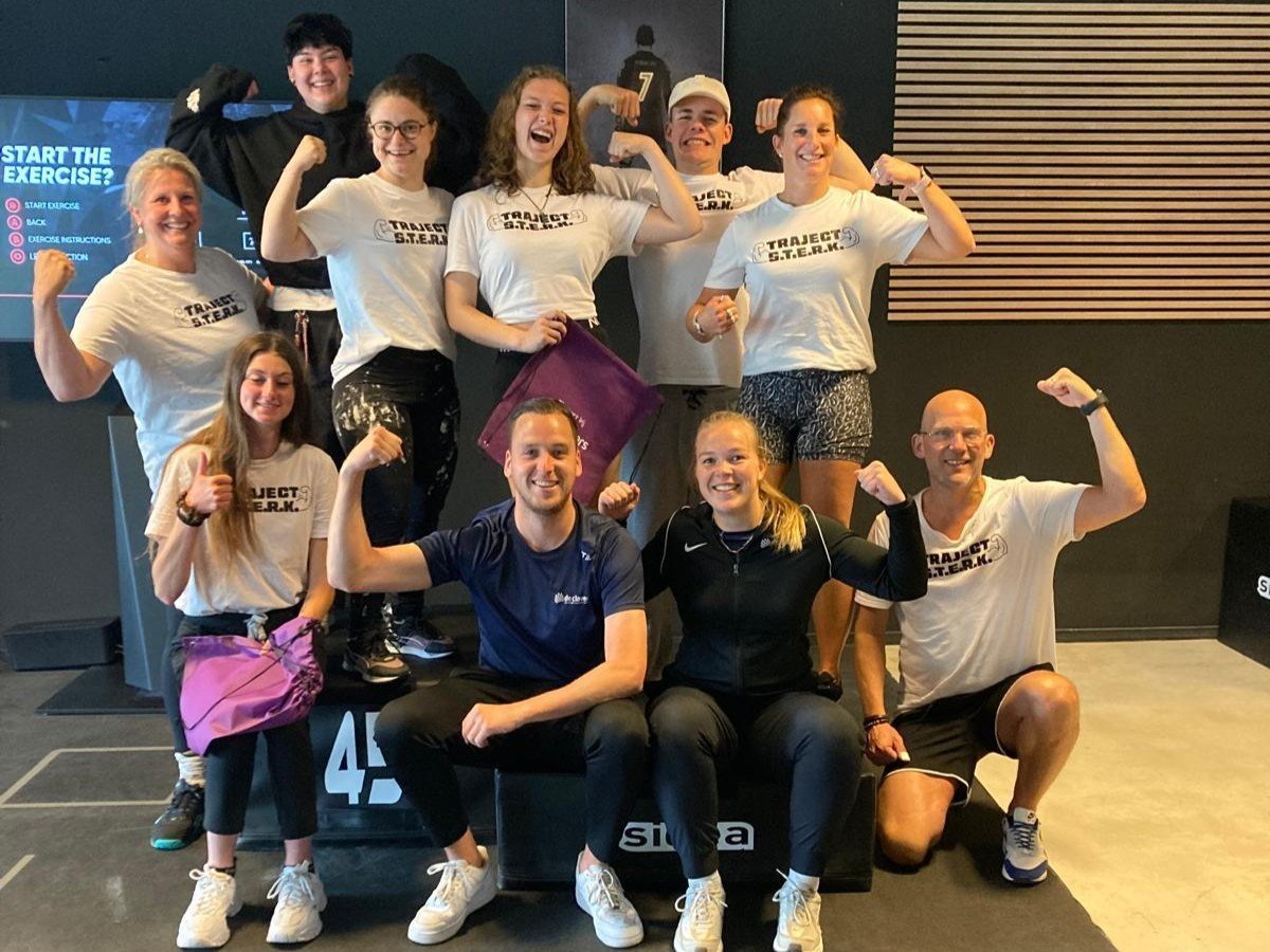 vrolijke groepsfoto van deelnemers en coaches van traject STERK laten in een gymzaal hun spierballen zien