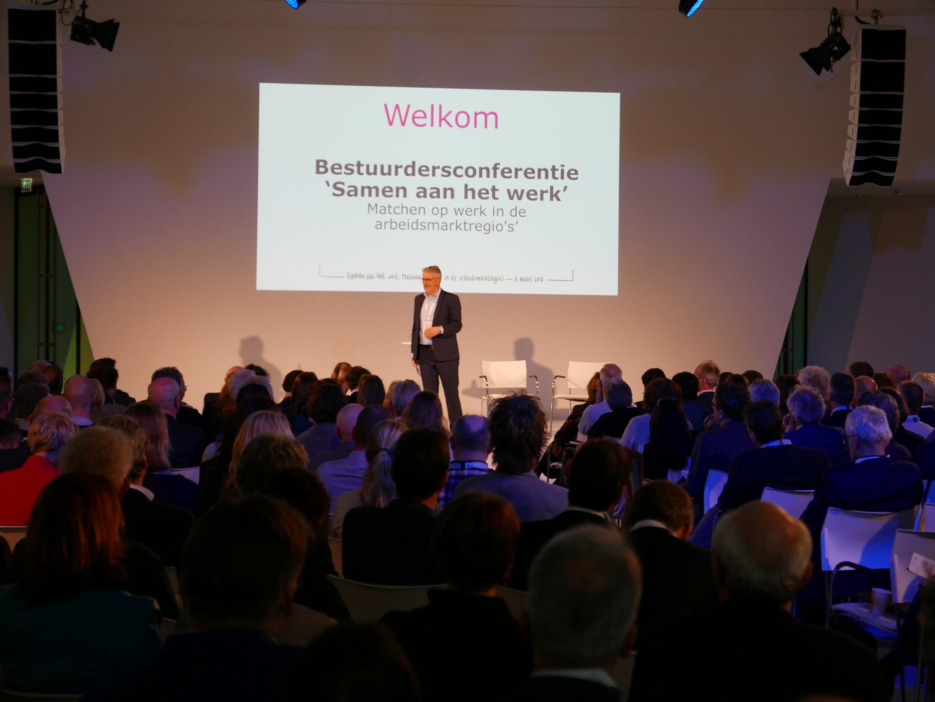 een persoon die op een podium staat voor een menigte mensen