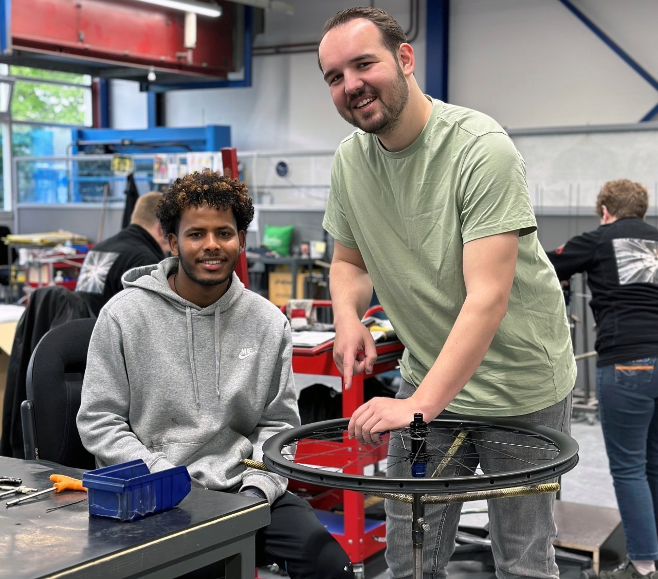 Twee jongemannen zijn in een werkplaats een fietswiel aan het repareren.