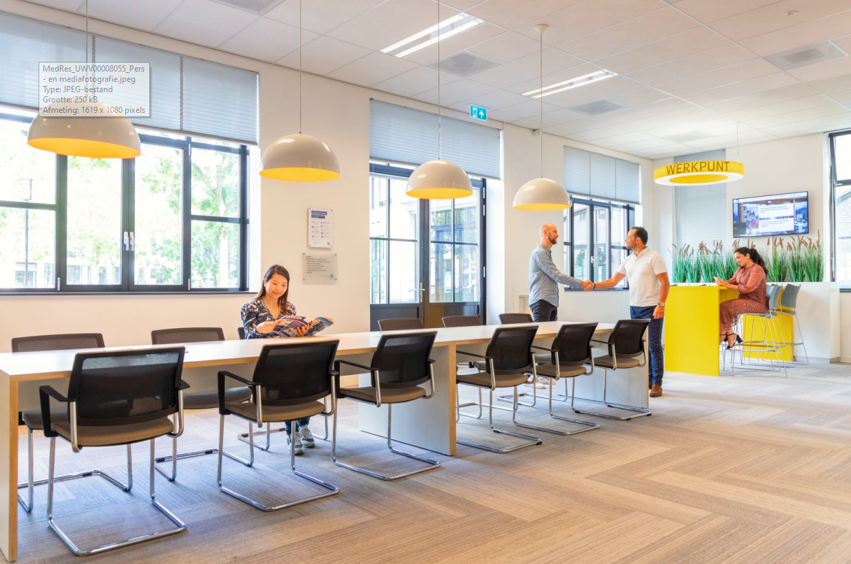 een ontvangstruimte van UWV. Iemand zit te wachte, een ander schudt de hand van een UWV-mdewerker en  een andere medewerker zit achter een bureau.