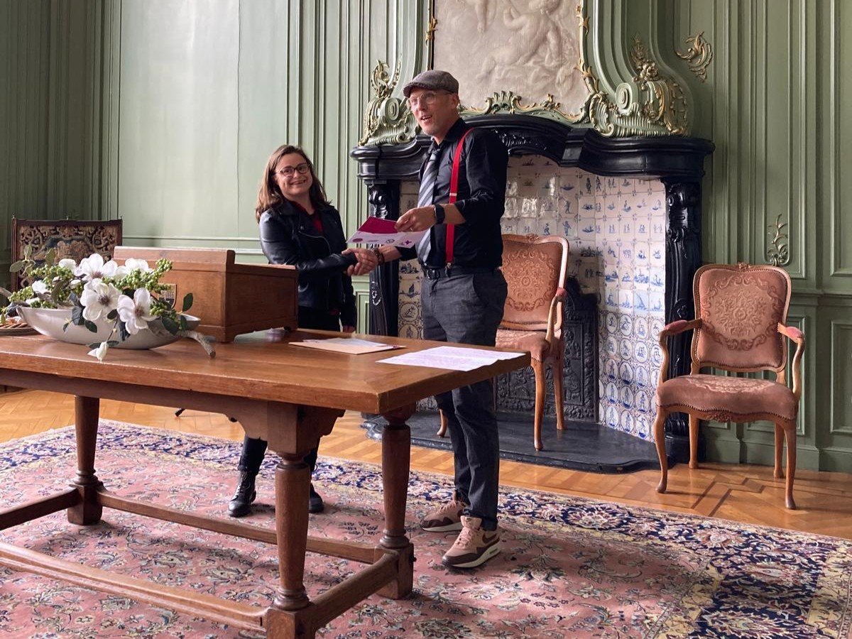 Brandyne krijgt haar MDT-certificaat uitgereikt in een deftige zaal door een man in het zwart met rode bretels en een pet