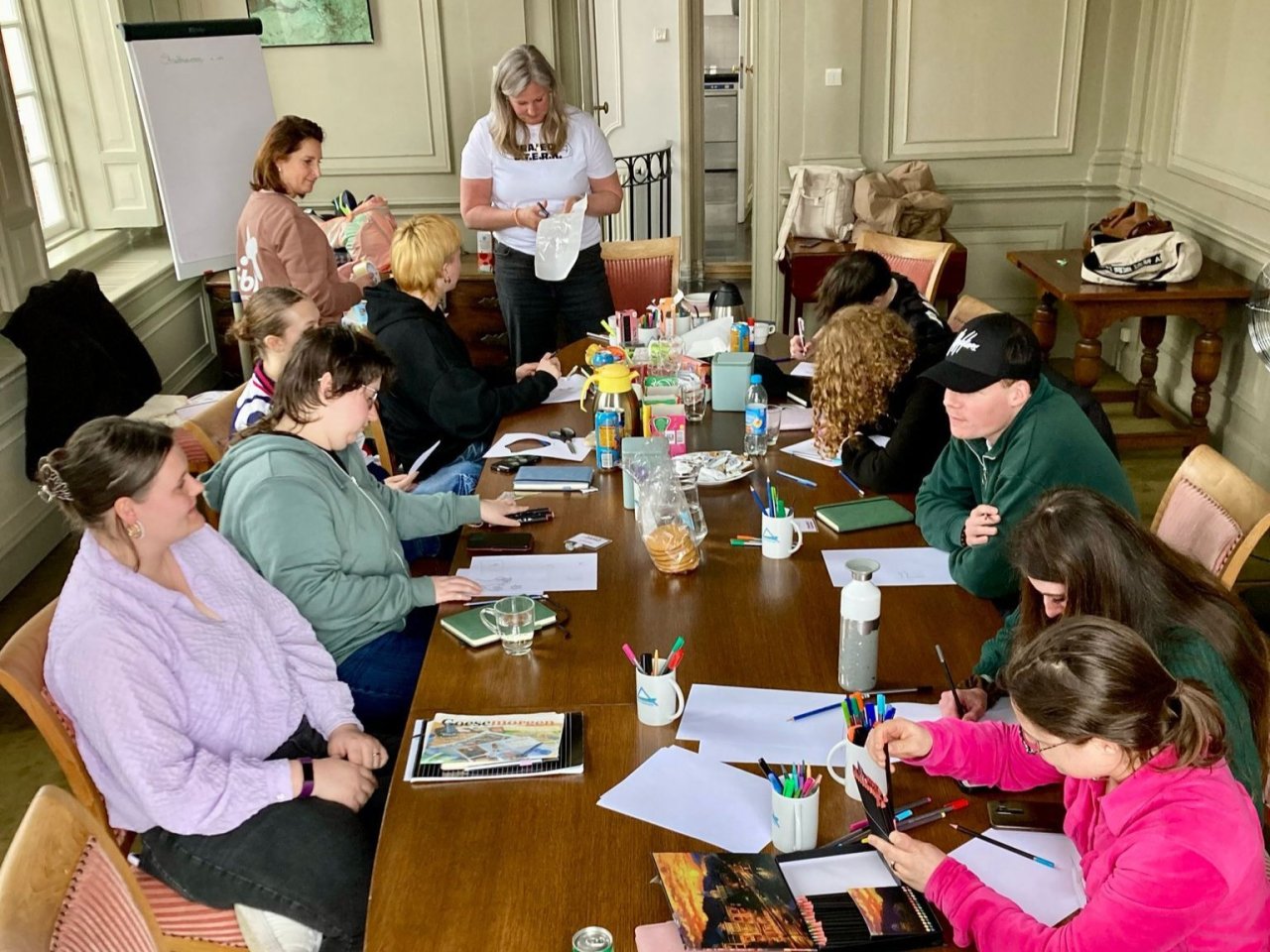 12 jongeren zitten rond een tafel en schrijven in een bulletjoural