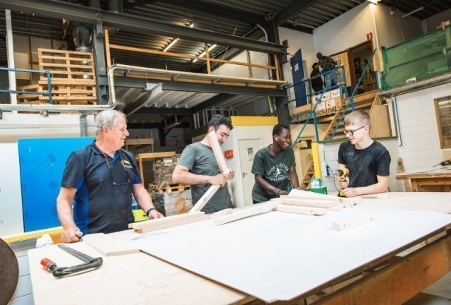 3 medewerkers bewerken hout; een begeleider kijkt toe