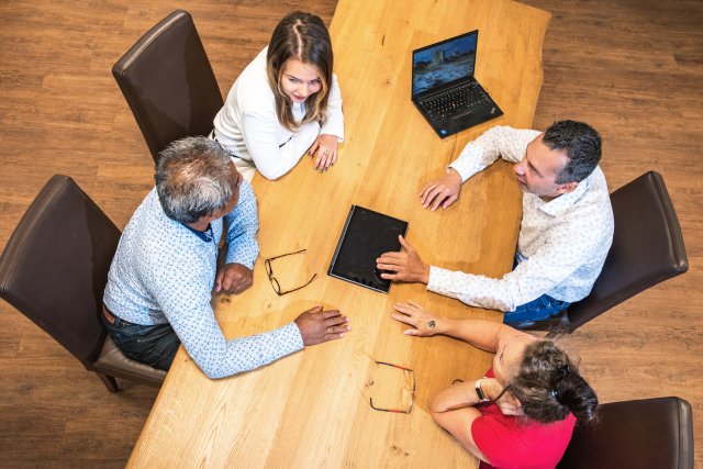 4 collega's aan tafel in gesprek, omringen 1 tablet